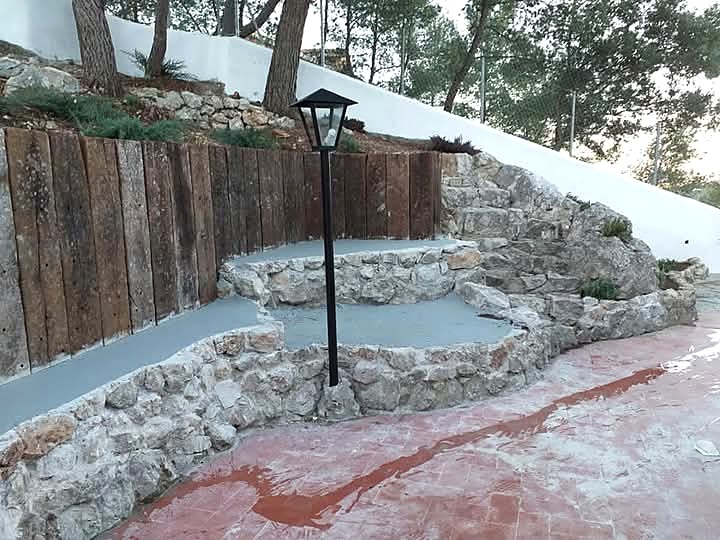 Terrazas de piedra y madera con iluminación en el jardín terminado
