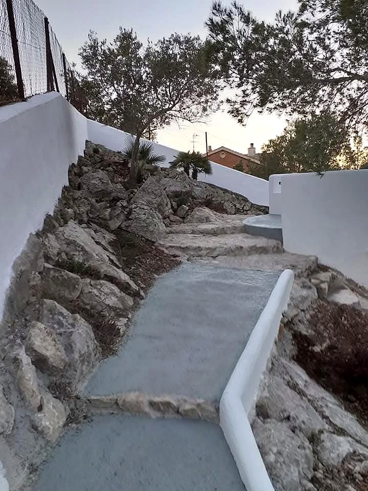 Camino ascendente entre roca y muros blancos en un jardín de Sitges